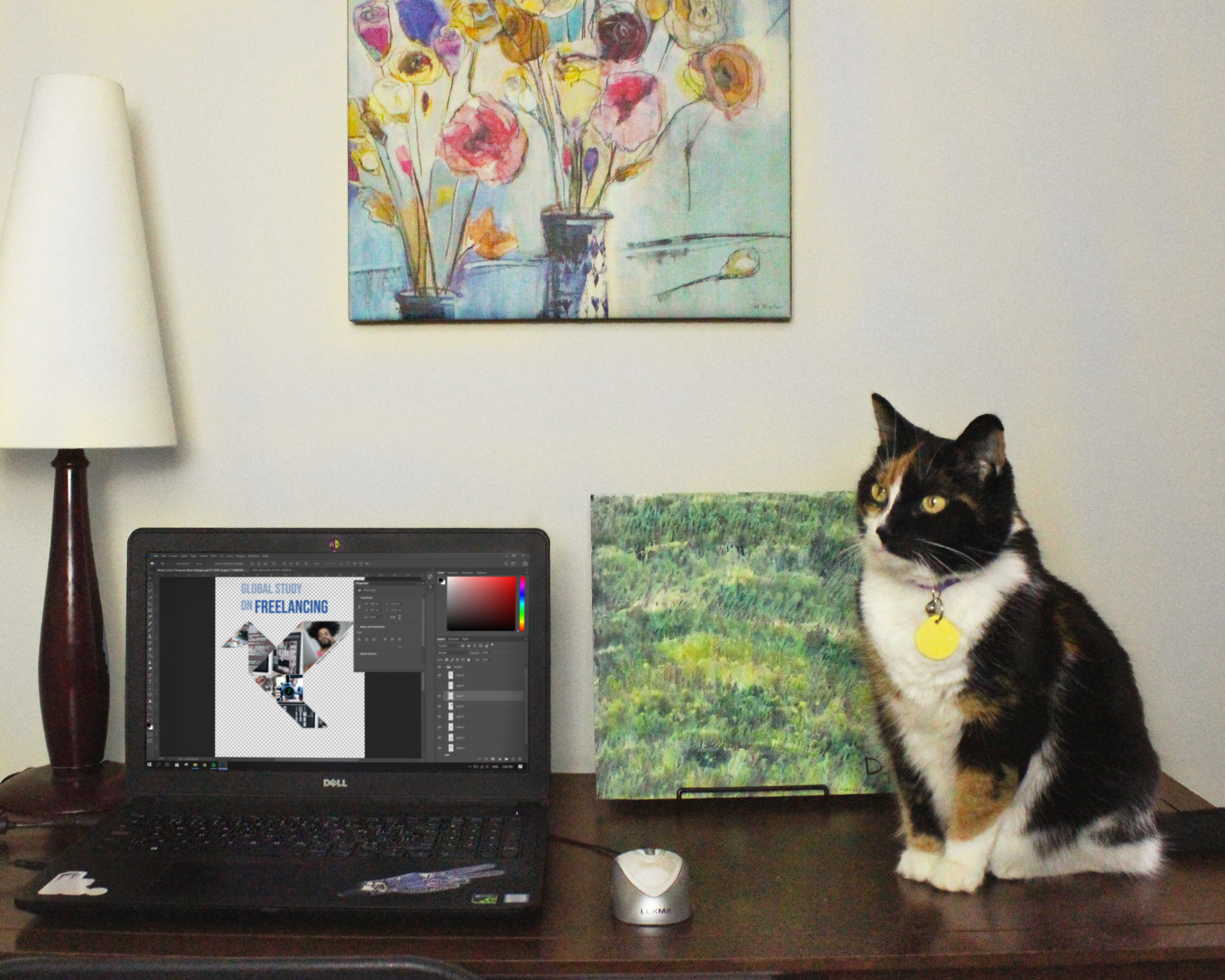 There is an office desk with a laptop and a cat on top. The laptop screen displays a logo being designed. The cat is seated and staring off in the distance.