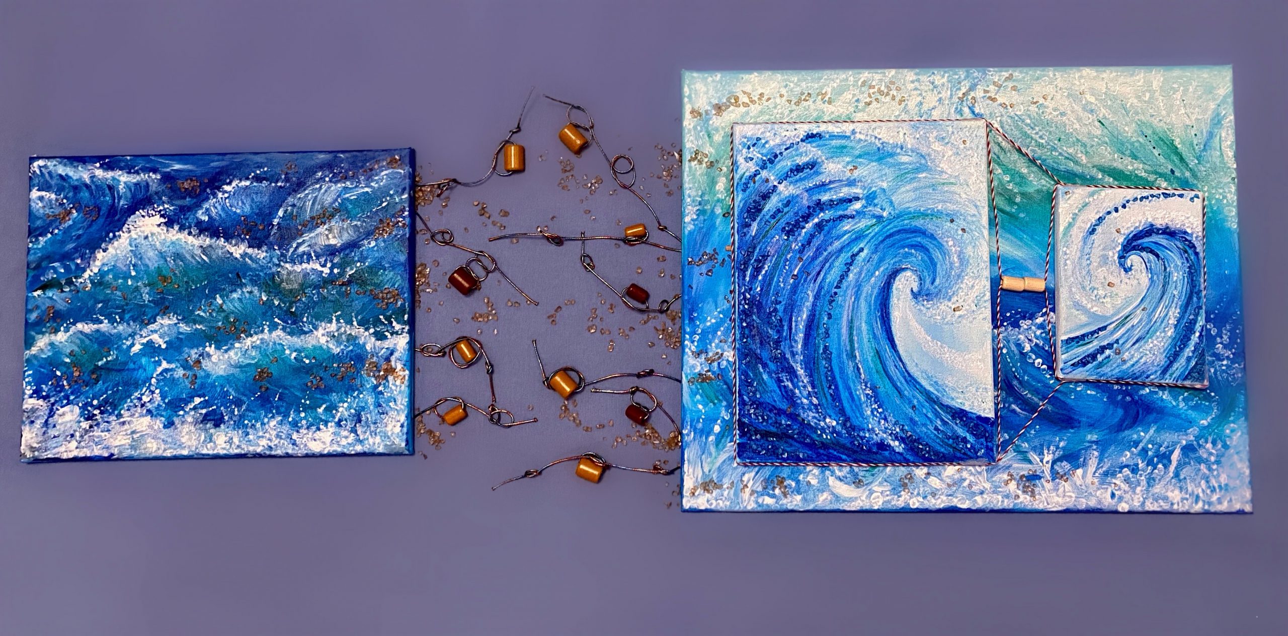 Two blue and white paintings represent the dynamic waves of the ocean. In between, are long elastics, wooden beads, and scattered gravel that almost connect them.